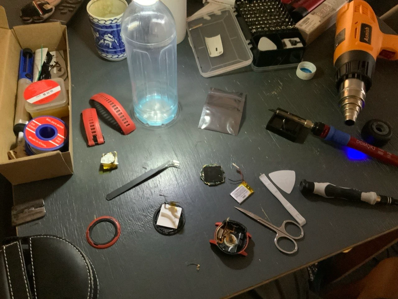 A broken sports watch taken apart on a workbench, surrounded by tools